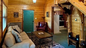 Ein gemütliches Blockhaus-Interieur mit Wohnzimmer, einer grünen Tür, einer Treppe und einer Küchenzeile.