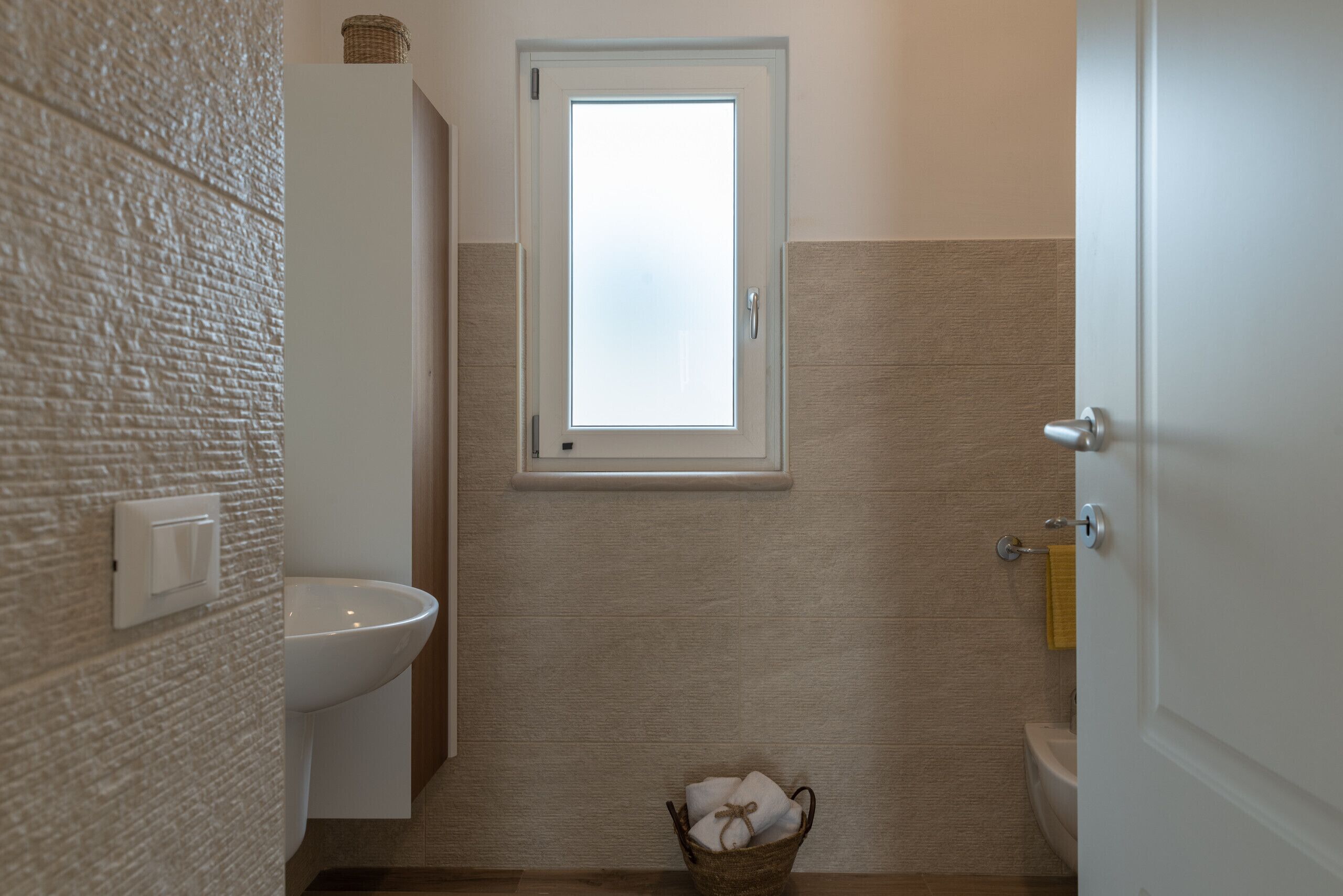 A bathroom with a white sink, a window, and a basket of towels.