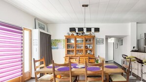 Un coin repas avec une table et des chaises en bois, un buffet en bois doté de portes en verre, et un espace cuisine comprenant un réfrigérateur et des tabourets de bar.