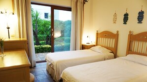 Une chambre d’hôtel avec deux lits, un bureau et une vue sur un jardin, accessible par une porte coulissante.
