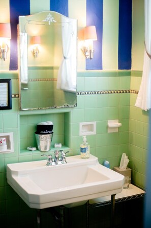 Un baño con lavamanos blanco, azulejos verdes, un espejo y dos lámparas fijadas a la pared.