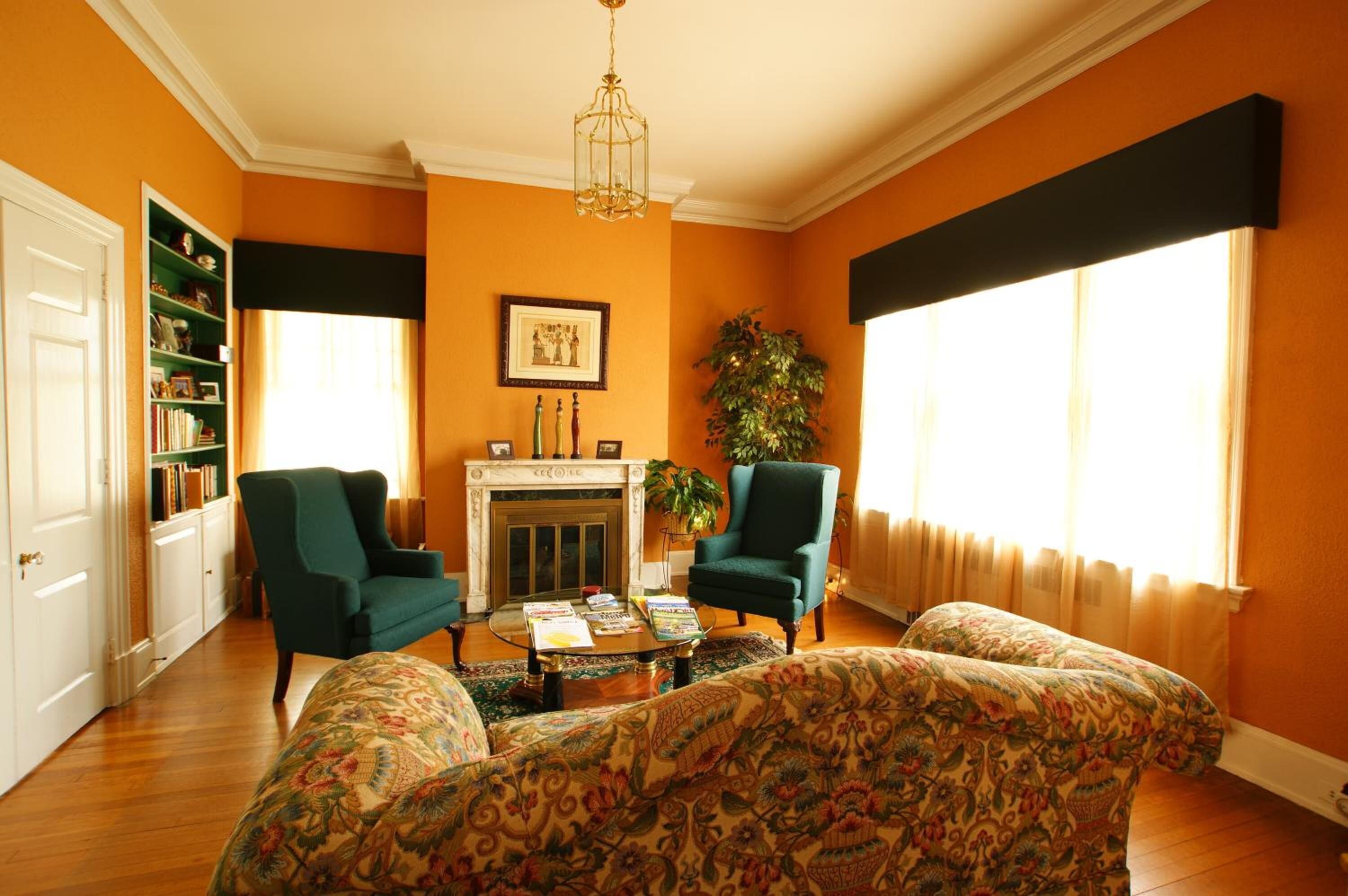 A living room with two green armchairs, a patterned sofa, a fireplace, and a bookshelf.