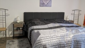 A bedroom with a bed, a nightstand, a lamp, a wall art piece, and a small table. - Apartment at the old Greetsieler Tief (Eilsum)