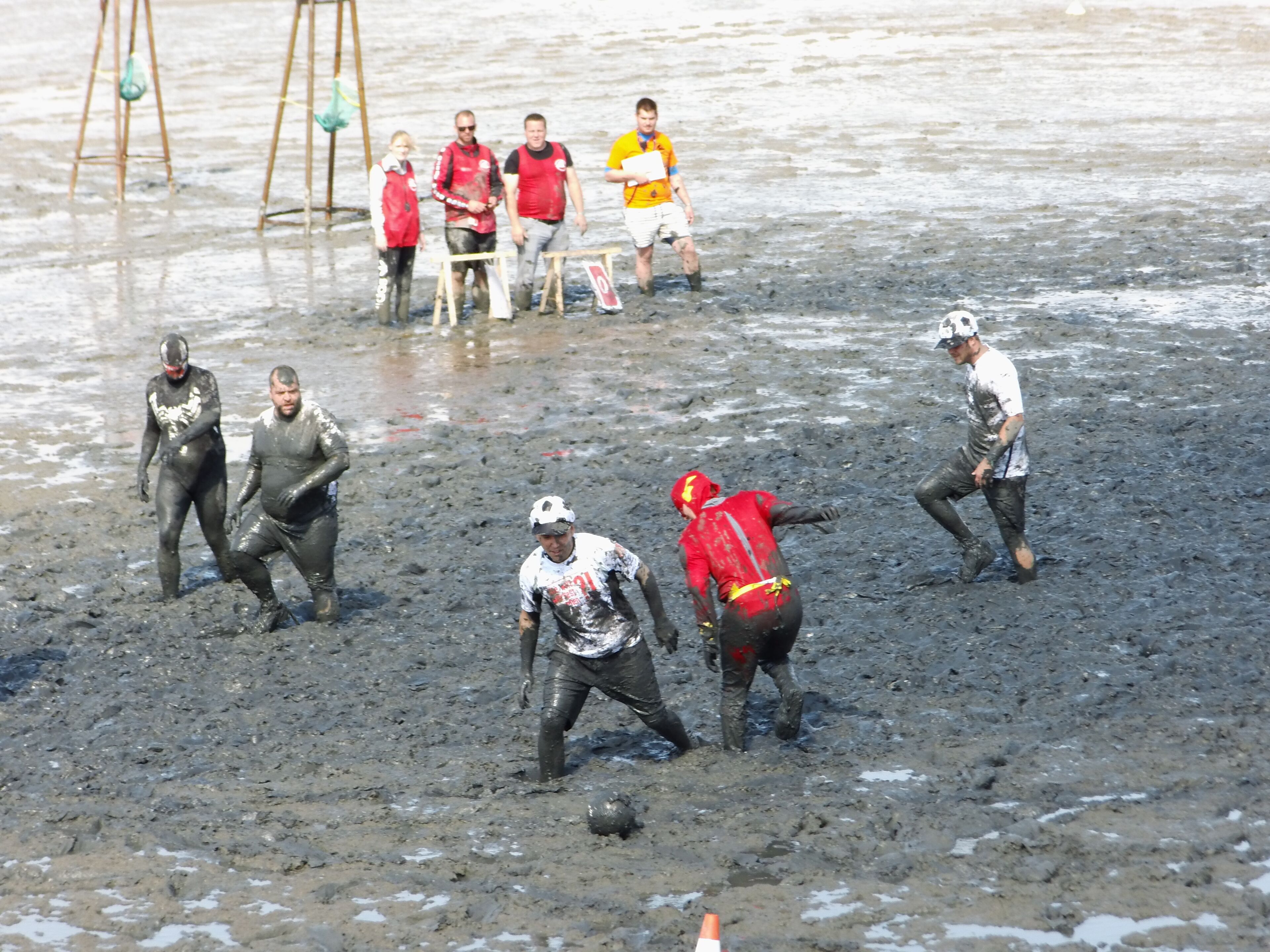 En gruppe mennesker spiller et sjovt spil i mudder på stranden.