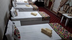 Une chambre d’hôtel avec quatre lits, chacun doté d’un matelas blanc et de couvre-lits à motifs floraux colorés.