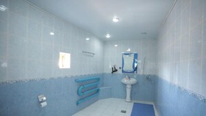 Une salle de bain avec des murs recouverts de carreaux bleus, un lavabo blanc, un miroir et un tapis bleu sur le sol.