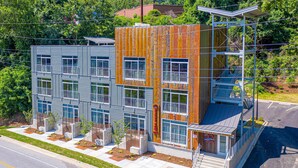 A modern multi-story building with a mix of metal and wood exterior, featuring balconies and a covered entrance. - Studio King Suite with Kitchen | 202 (Asheville)