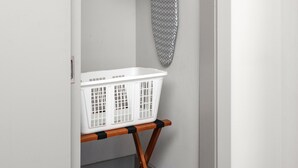 A laundry area with a white basket, wooden hanger, and an ironing board. - Studio King Suite with Kitchen | 202 (Asheville)