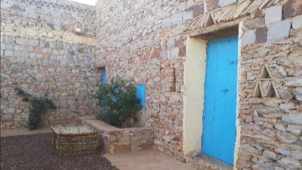 Ein gepflasterter Innenhof mit einer blauen Tür, einem kleinen Garten und einem Holzstoß.