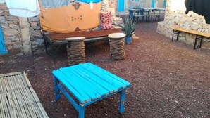 Ein Sitzbereich im Freien mit einem blauen Tisch und Bänken, umgeben von Säulen und einer überdachten Sitzgelegenheit.