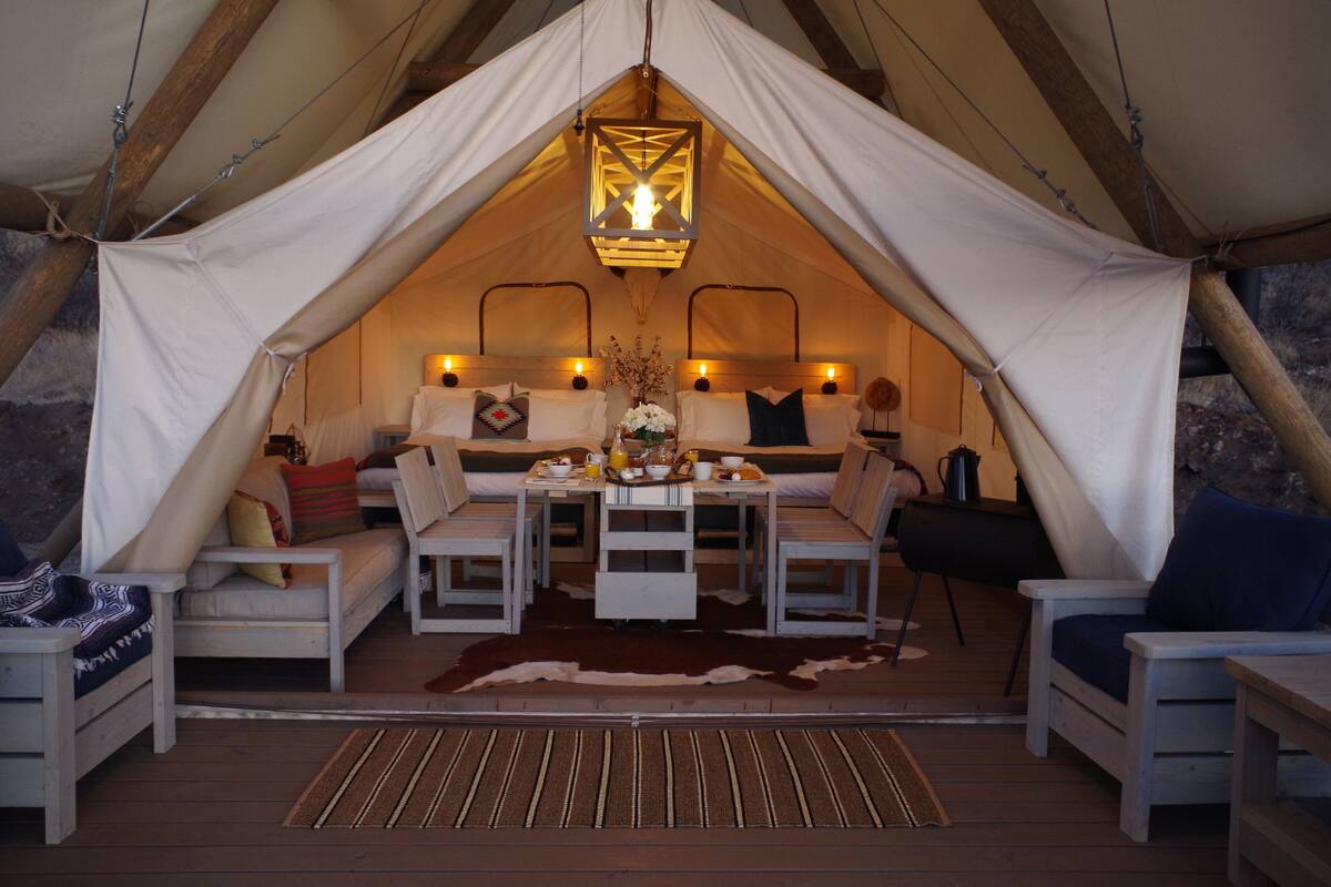 A cozy tent with a central table, two sofas, and a hanging light fixture.