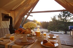 A breakfast setup in a tent with a table, breakfast items, and a view of trees and hills. - Black Tree Resort (Lake George)