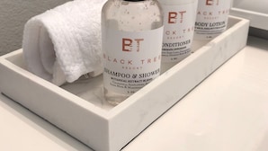 A bathroom shelf with three bottles of Black Tree Resort products: a shampoo and shower, a conditioner, and a body lotion. - Black Tree Resort (Lake George)