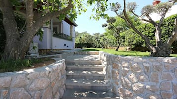 Una scala in pietra conduce a un edificio bianco con un balcone, circondato da alberi e un'area verde.