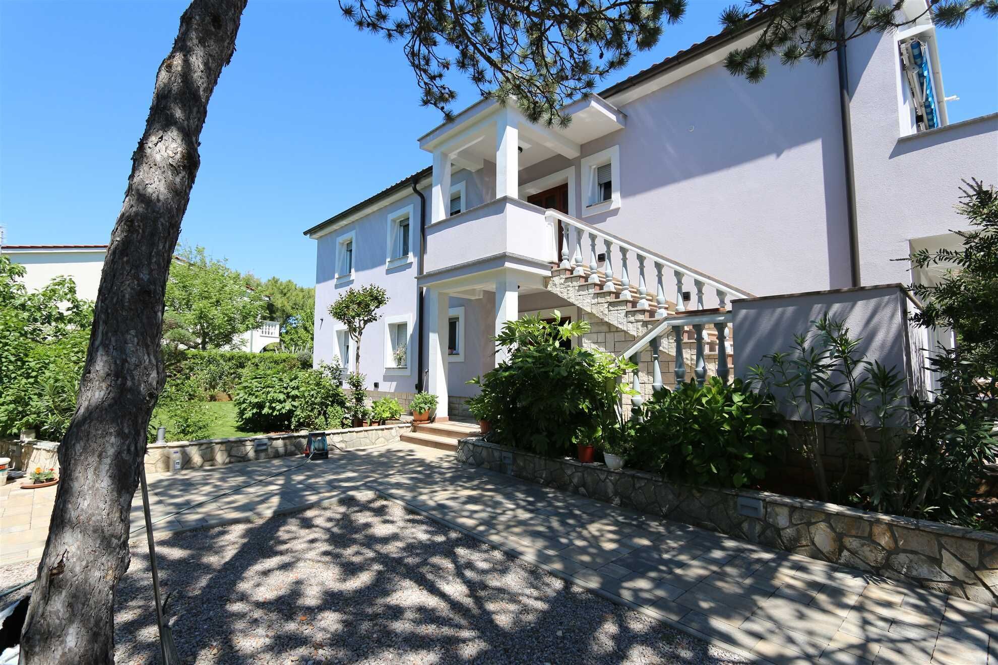 Una casa a due piani con una scala in pietra, un portico coperto e un vialetto sterrato.