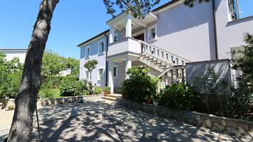 Una casa a due piani con una scala in pietra, un portico coperto e un vialetto sterrato.