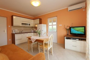 Un espace de vie compact comprenant un coin cuisine, un coin repas avec une table et des chaises, un téléviseur et une porte dotée de panneaux en verre dépoli.
