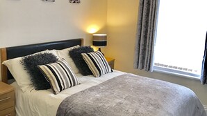 A neatly made bed with striped pillows, a bedside lamp, and a window with curtains. - Hawthorn House (Blackpool)