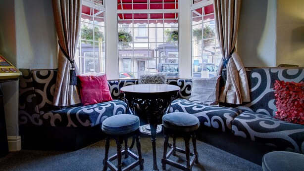 A bay window seating area with a round table and two stools, patterned cushions, and a view of the street. - Hawthorn House (Blackpool)