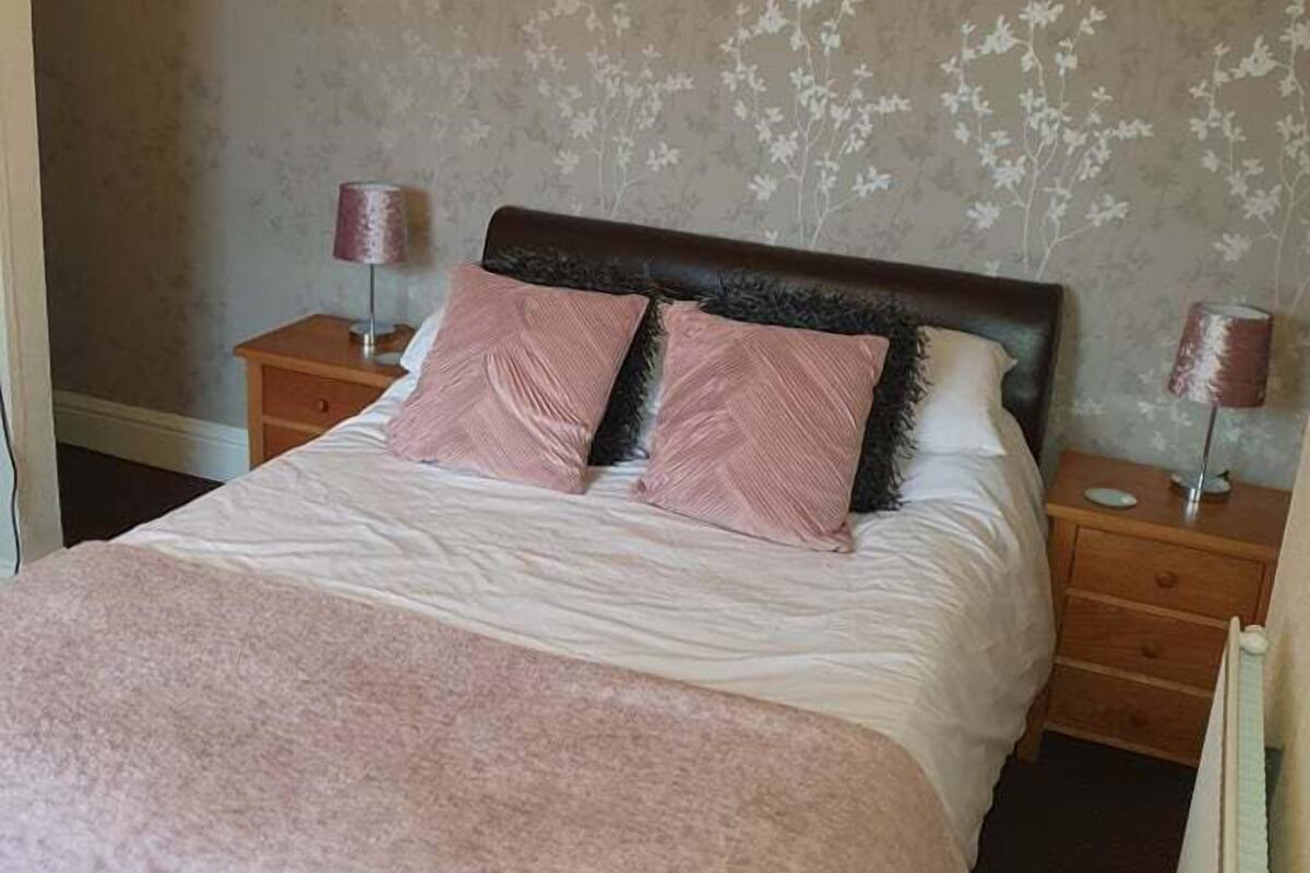 A neatly made bed with a pink blanket and two matching pillows, flanked by two bedside tables with lamps.