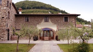 Un edificio de piedra con una entrada central, un pequeño patio y vistas a una colina al fondo.