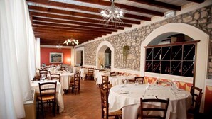 Un restaurante con varias mesas y sillas, paredes de piedra y suelo de baldosas.