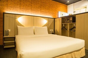 A hotel room with a large bed, wooden wardrobe, and a brick wall. - Onomo Tanger Med (Ksar El Majaz)