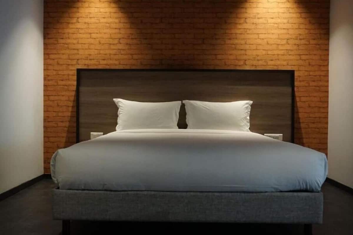 A bed with a headboard against a brick wall, a bedside table, and a wall-mounted light.