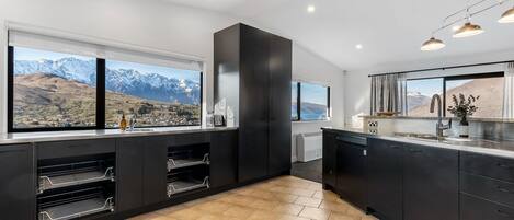 Una cocina moderna con armarios oscuros, un amplio ventanal con vistas a la montaña y un horno empotrado.