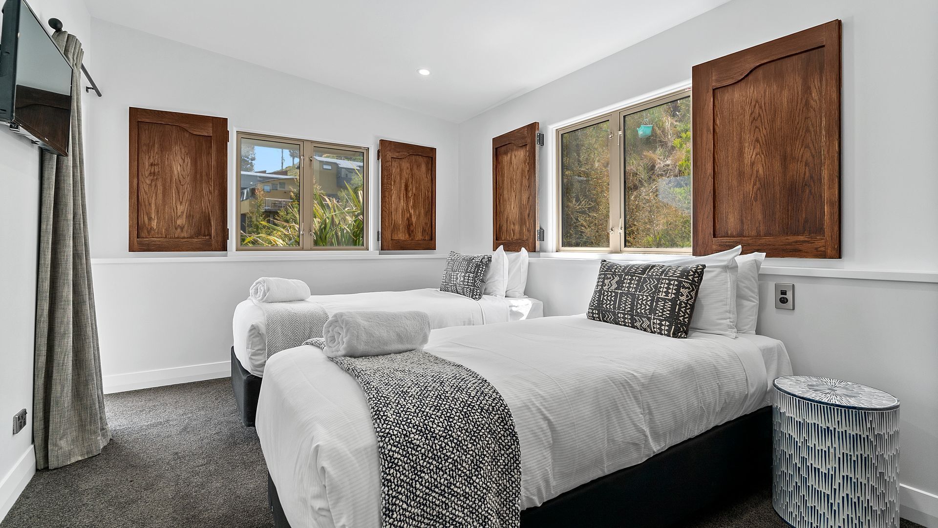 A hotel room with two beds, large windows, wooden shutters, and a small round side table.