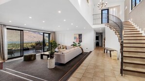 Ein großzügiger Wohnbereich mit einer großen Couch, einem Couchtisch und einer Zimmerpflanze. Eine Treppe führt auf eine obere Ebene.