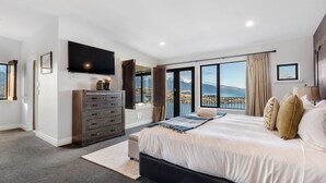 Ein Schlafzimmer mit einem großen Bett, einer Kommode, einem Fernseher und einem Balkon mit Blick auf die Berge.