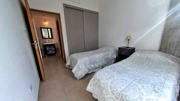 A bedroom with two beds, a wardrobe, a bedside table with a lamp, and a bathroom visible through an open door.