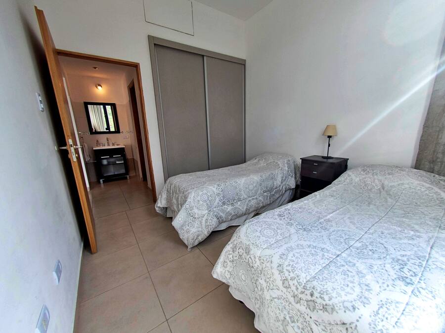 A bedroom with two beds, a wardrobe, a bedside table with a lamp, and a bathroom visible through an open door.