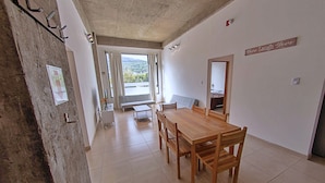 Een eetgedeelte met een houten tafel en stoelen, een bankje en uitzicht op een balkon met gordijnen.