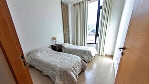 Een slaapkamer met twee bedden, een nachtkastje, een raam met gordijnen en uitzicht naar buiten.