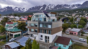 Un edificio moderno de varios pisos, situado en un pueblo con montañas al fondo.