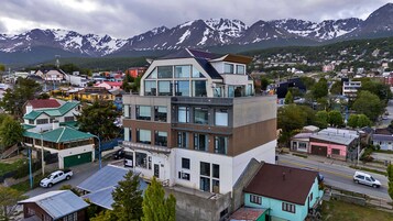 Un edificio moderno de varios pisos, situado en un pueblo con montañas al fondo.