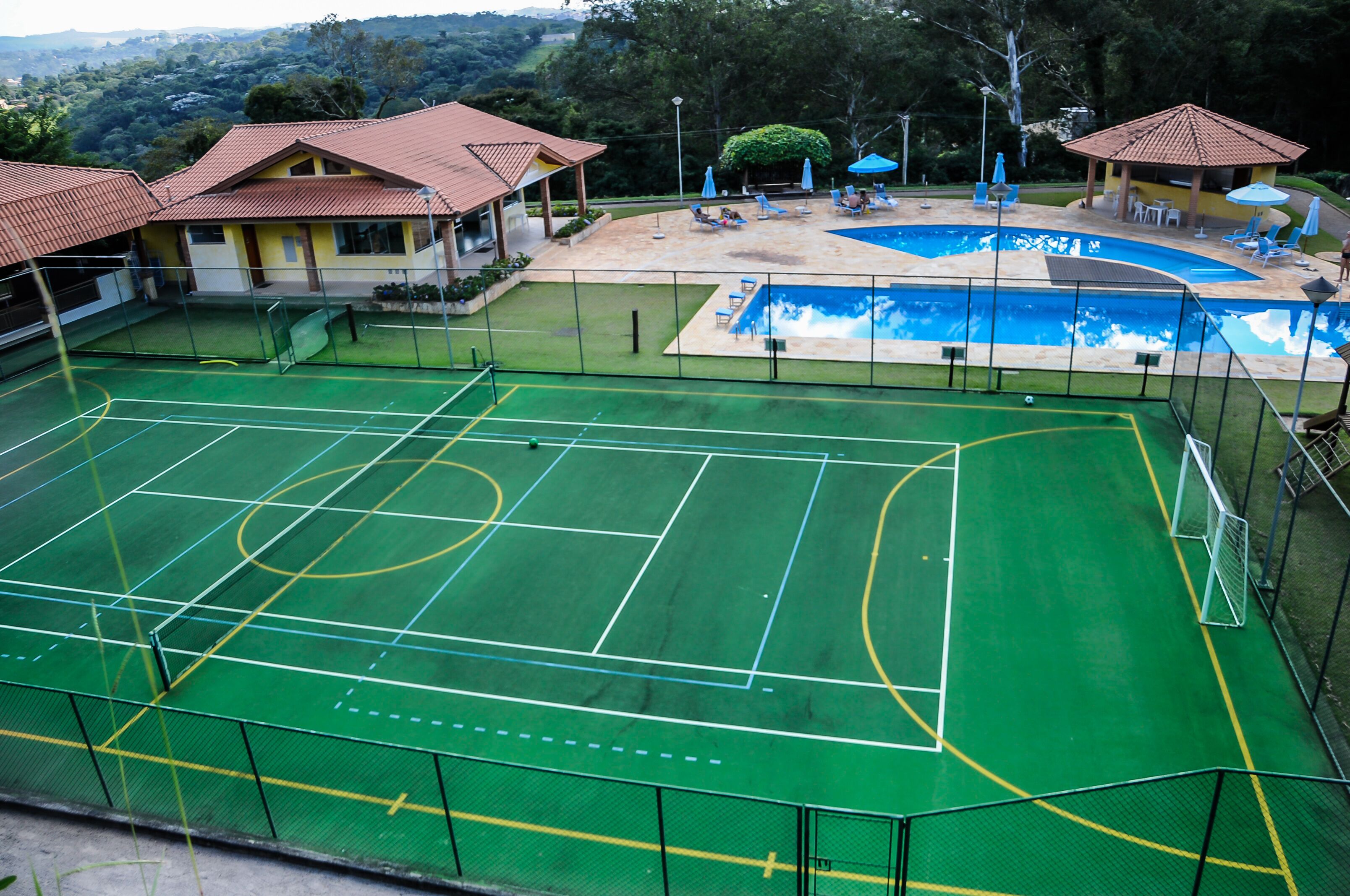 A sports facility with a tennis court, a swimming pool, and a covered seating area.