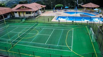 A sports facility with a tennis court, a swimming pool, and a covered seating area.