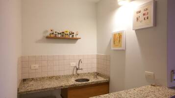 Un baño con lavamanos de encimera de granito, tocador de madera y repisa con adornos.