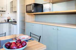 A compact kitchen with a microwave, a bowl of apples, and a dining table.