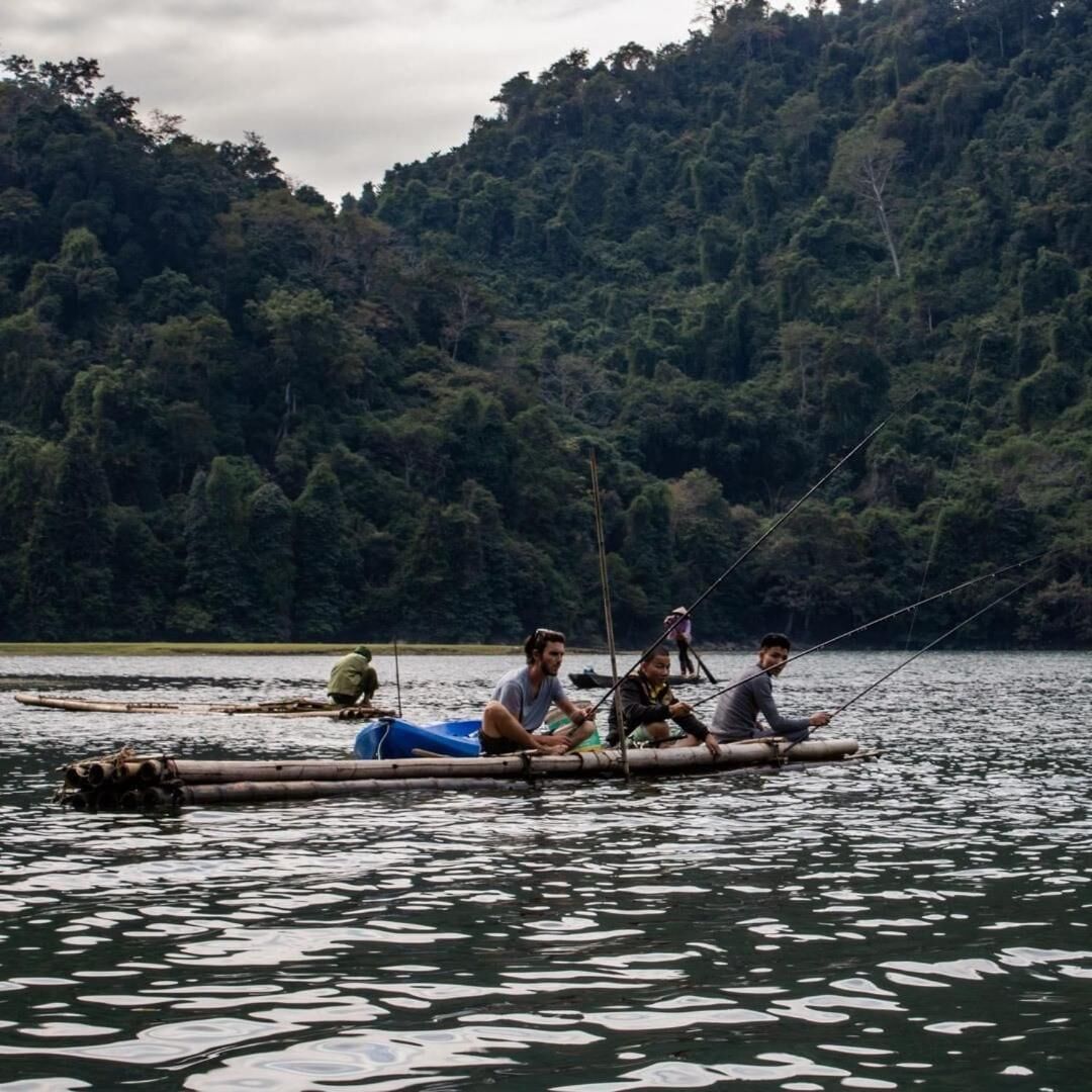 Un grupo de personas en una balsa de bambú sobre aguas tranquilas, rodeado de un bosque denso.