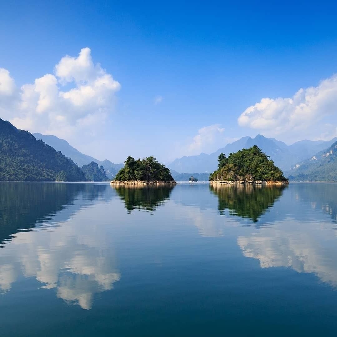 A tranquil lake with two small islands, surrounded by mountains under a clear sky.