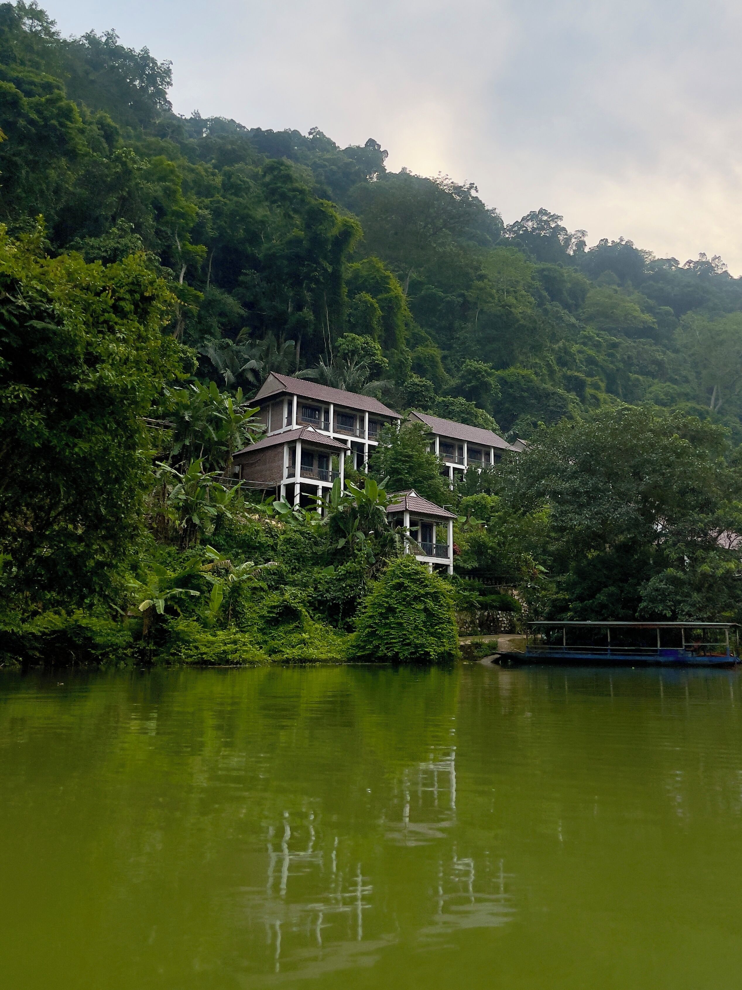 A building with a balcony, surrounded by lush greenery and a body of water.