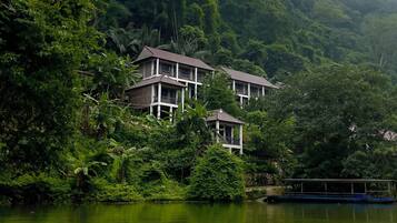A building with a balcony, surrounded by lush greenery and a body of water.