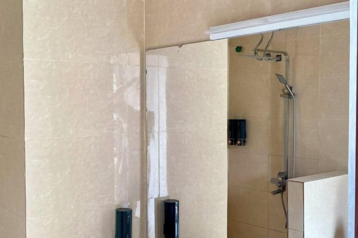 A bathroom with beige tiles, a shower with a handheld showerhead, and a white door frame.
