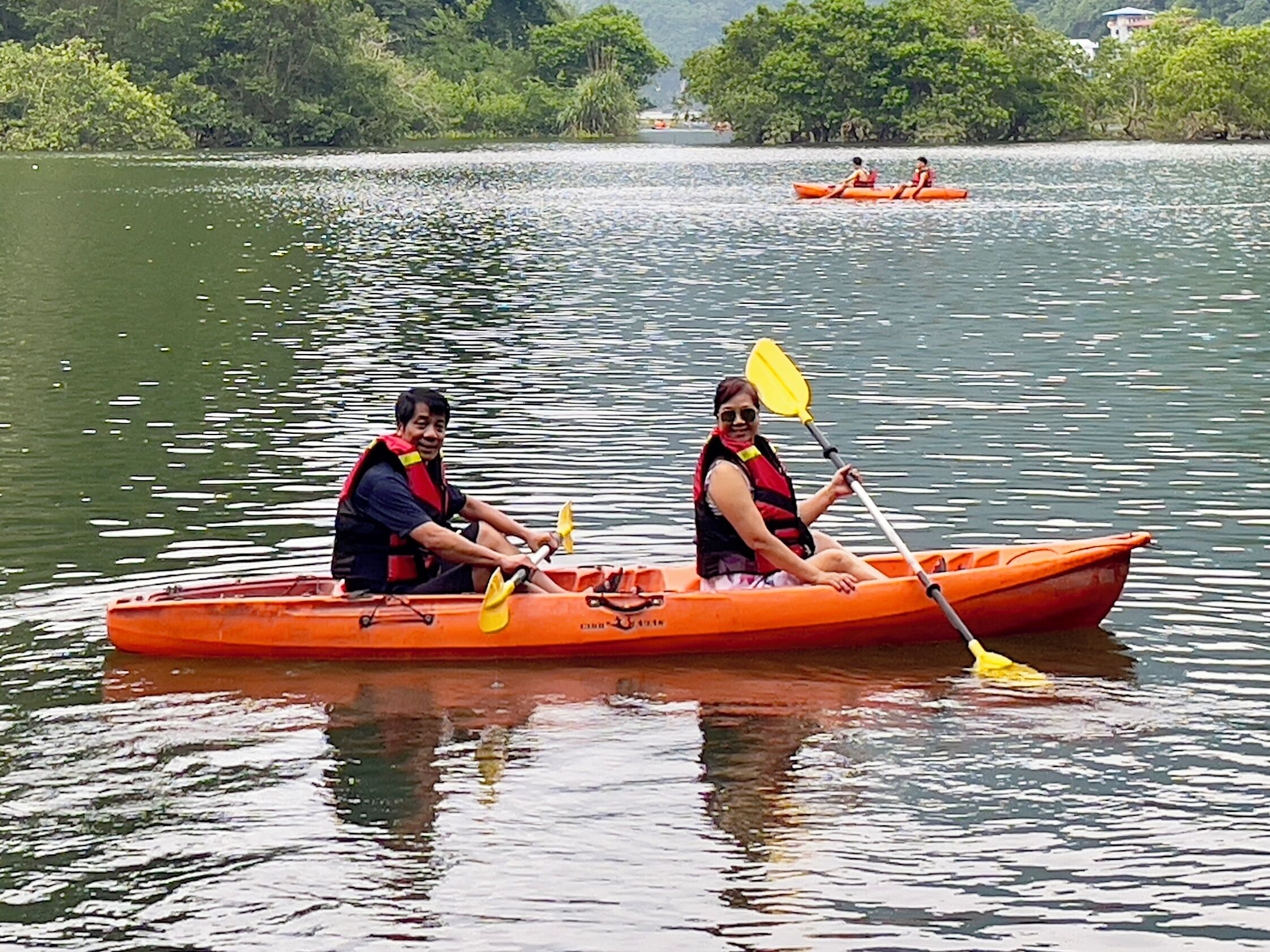 Two people in an orange canoe on a calm lake with trees in the background.