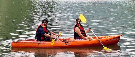 Two people in an orange canoe on a calm lake with trees in the background.