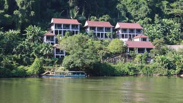 A row of white buildings with red roofs, surrounded by lush greenery and a body of water.